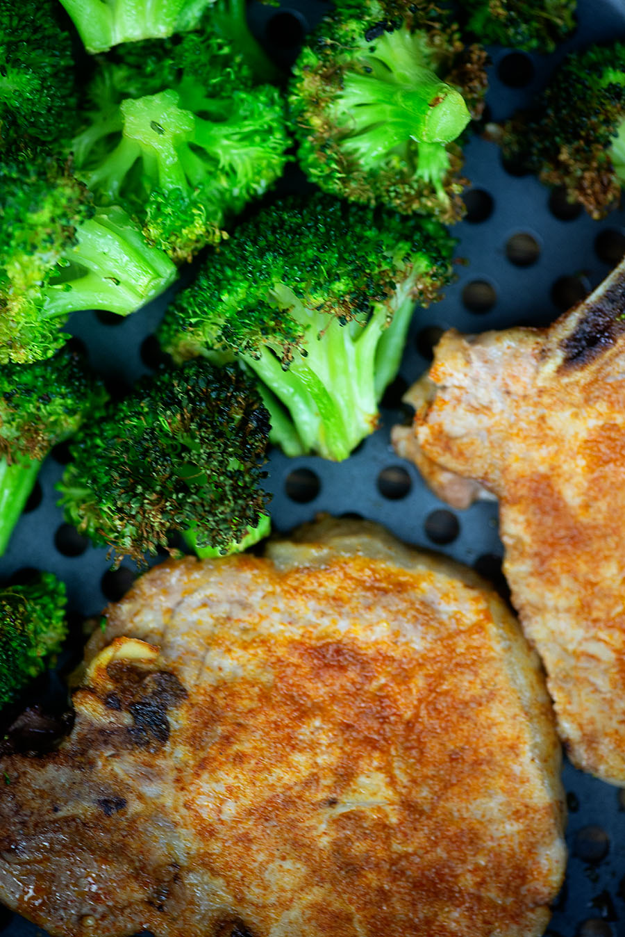 cooked broccoli and pork chops in an air fryer pan