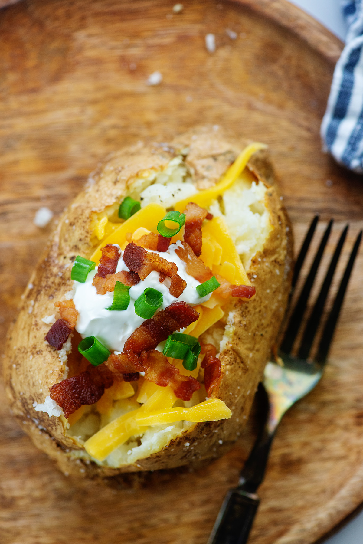 A loaded baked potato and a fork on a wooden cutting board.