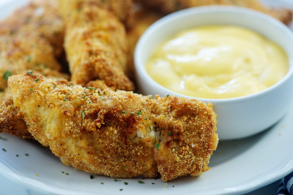 Chicken tenders on a white plate next to a white dipping dish.