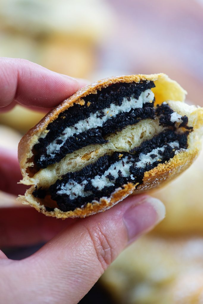 A woman holding a fried oreo cut in half up to the camera.