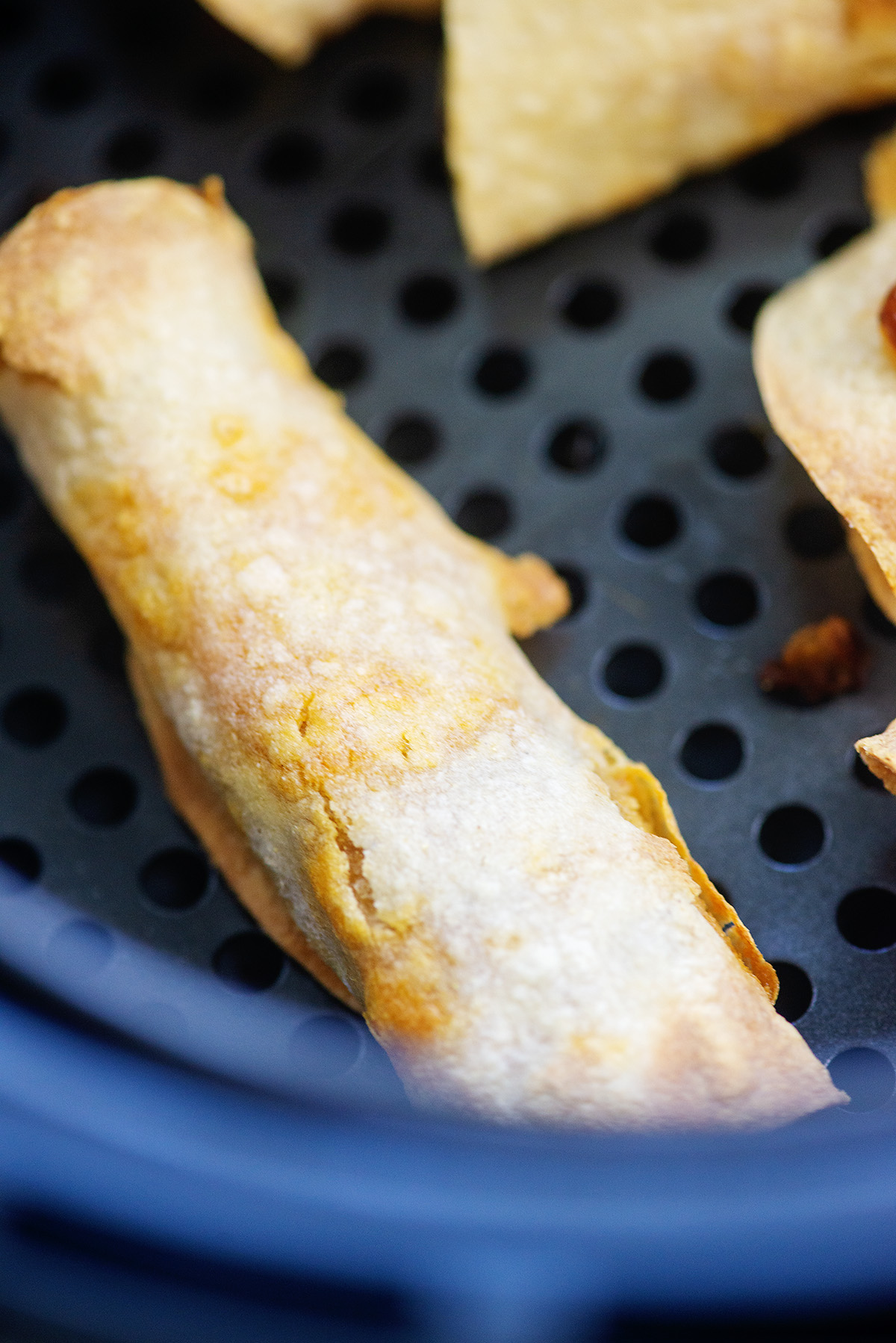 A close up of a cooked taquito in an air fryer basket.