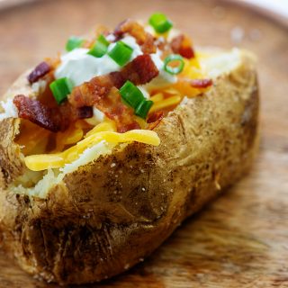 A baked potato topped with bacon and shredded cheese on a potato.