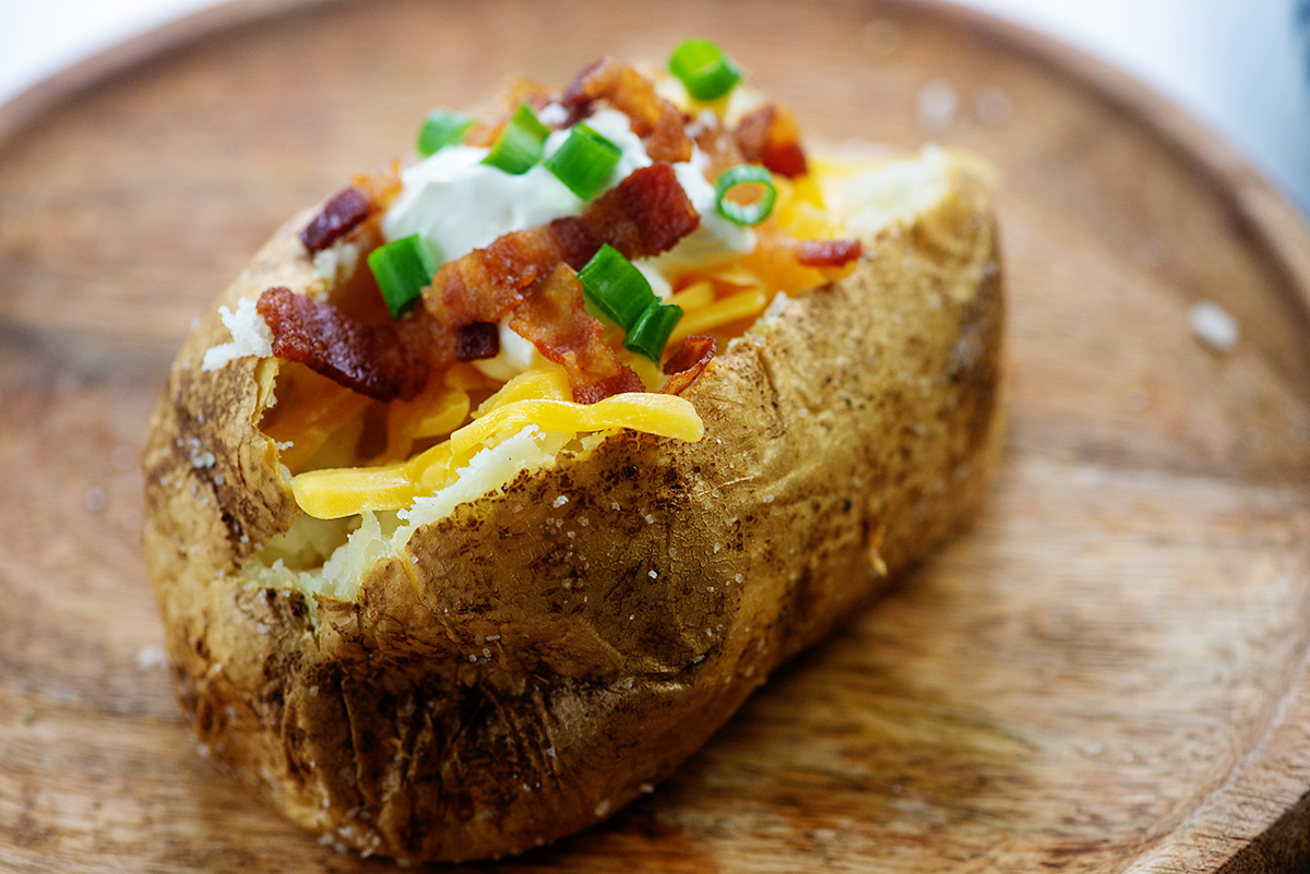 A baked potato topped with bacon and shredded cheese on a potato.