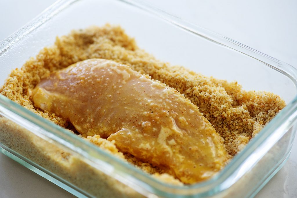 Raw chicken tenders dipped into breading.