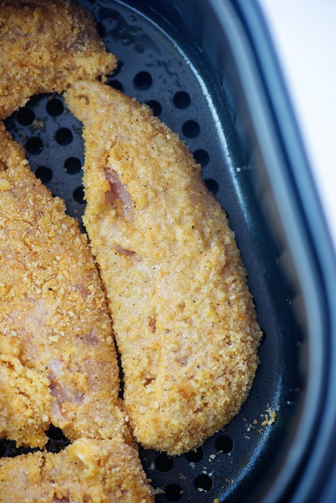 Uncooked chicken tenders in an air fryer pan.