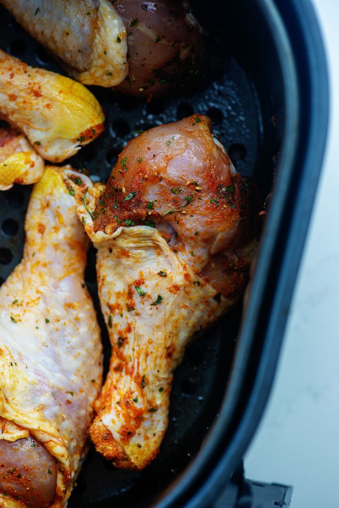 Seasoned raw chicken legs in an air fryer pan.