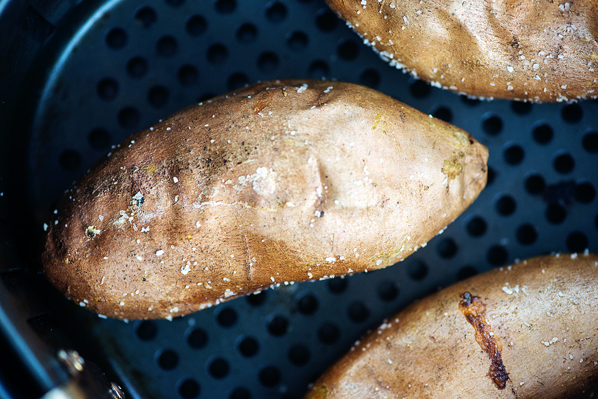 Three whole sweet potatoes in an air fryer basket.