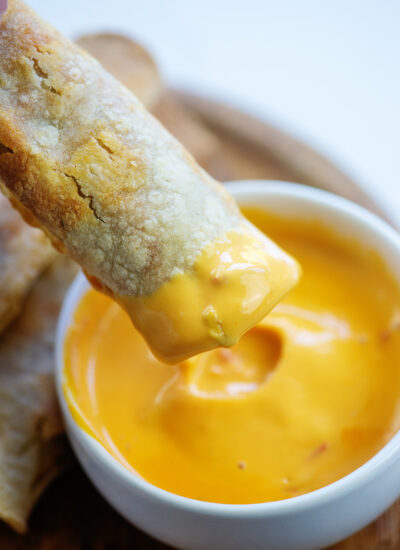 A taquito being dipped into a cheese sauce