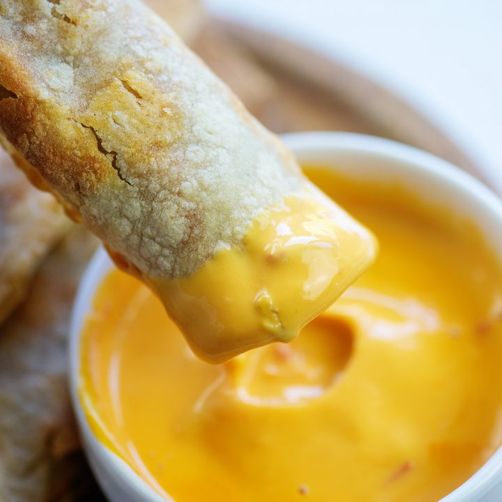 A taquito being dipped into a cheese sauce