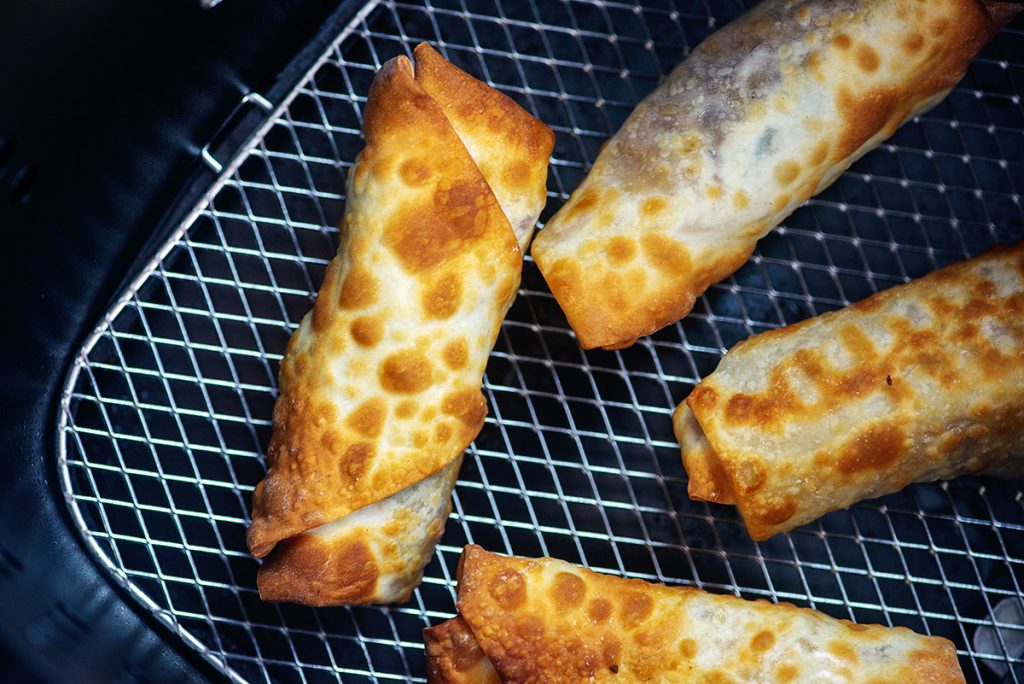 Overhead view of cooked egg rolls in an air fryer basket