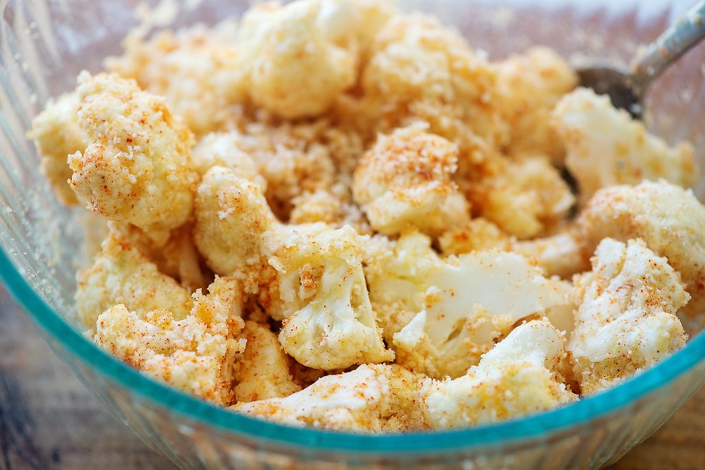 A close up of breaded cauliflower being stirred in a clear glass bowl