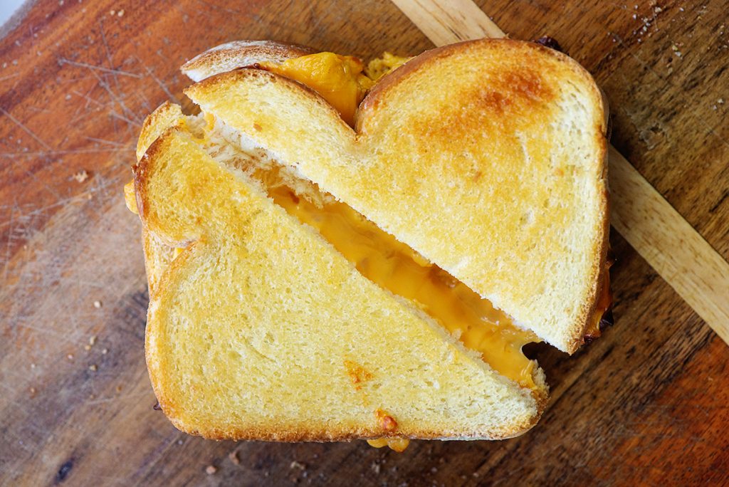 cheesy grilled cheese sandwich on wooden cutting board