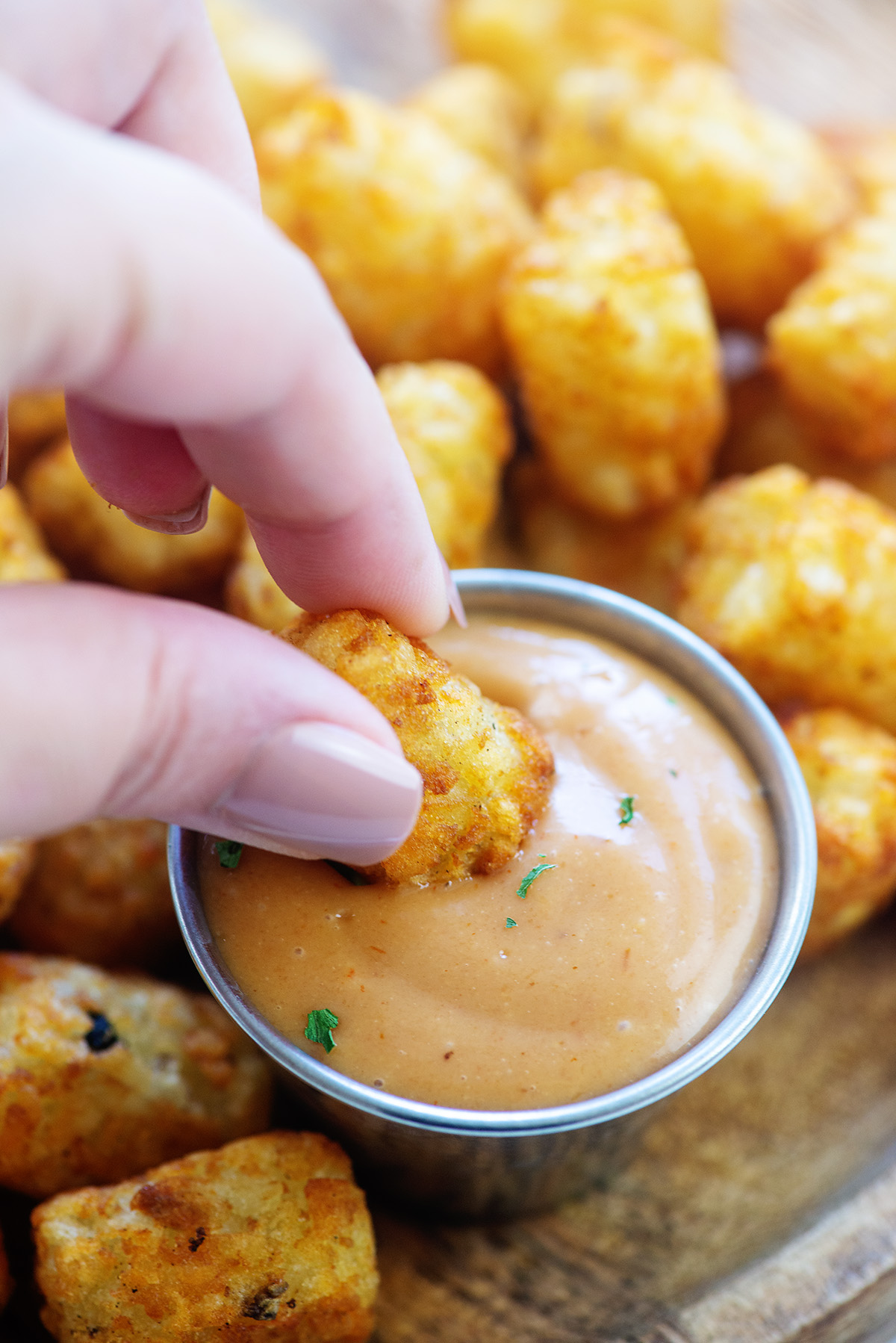 A woman dipping tater tots into a cup of tater tot dip.