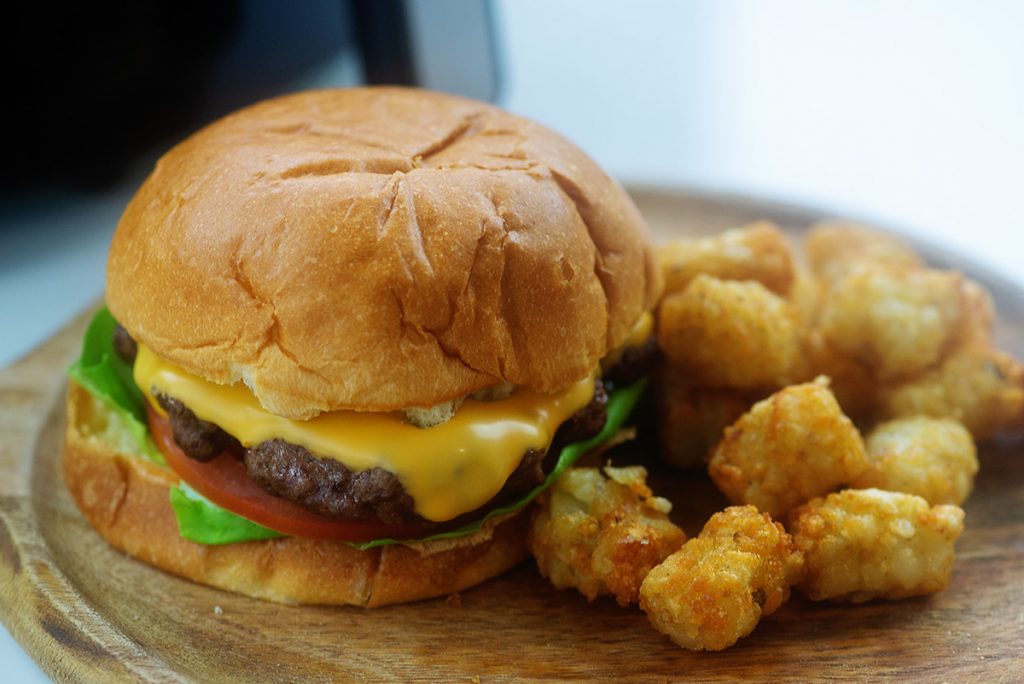 A cheeseburger and tater tots on a wooden plate