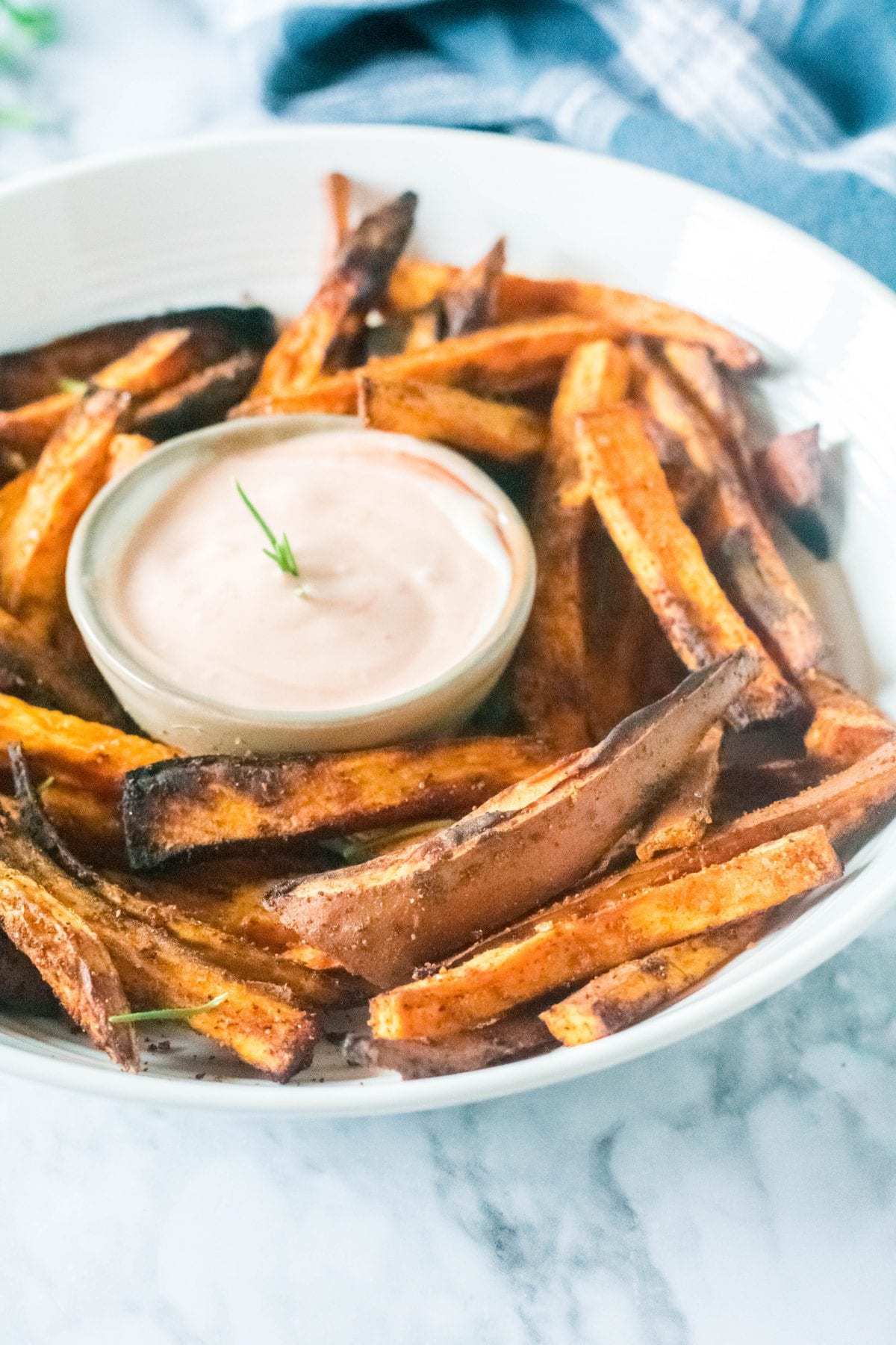 Sweet potato fries in a white bowl around a cup of dip