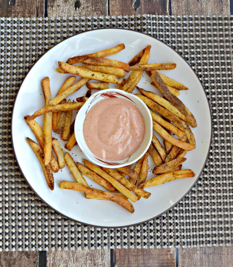 French fries and a cup of sauce on a white plate.