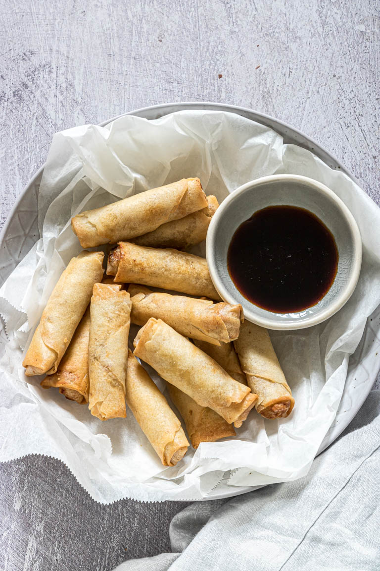 Overhead views of a pile of egg rolls on a plate.