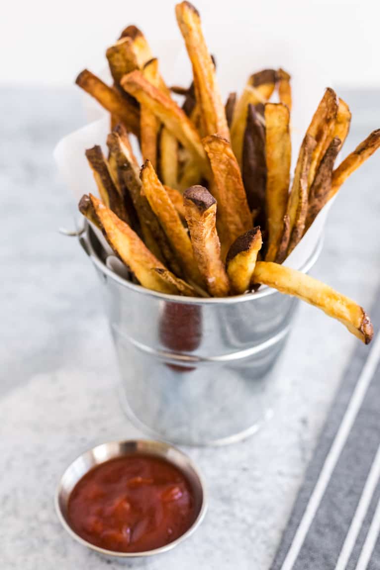 French fries standing up in a metal cup next to a cup of ketchup
