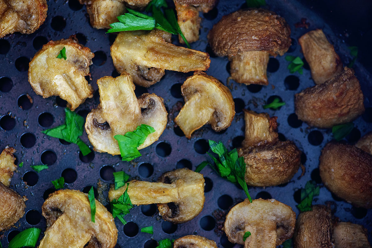 Mushrooms cooked with garlic butter spread out in an air fryer basket.