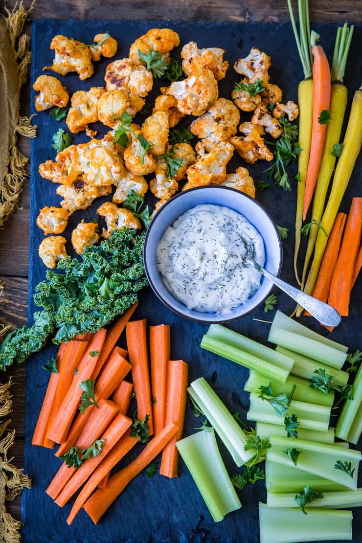 A bunch of veggies on a cutting board surrounding a cup of ranch dip.
