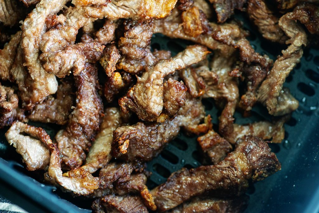 cooked beef strips in an air fryer basket.