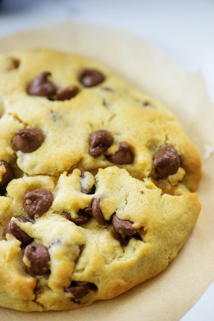 A close up of a chocolate chip cookie on wax paper