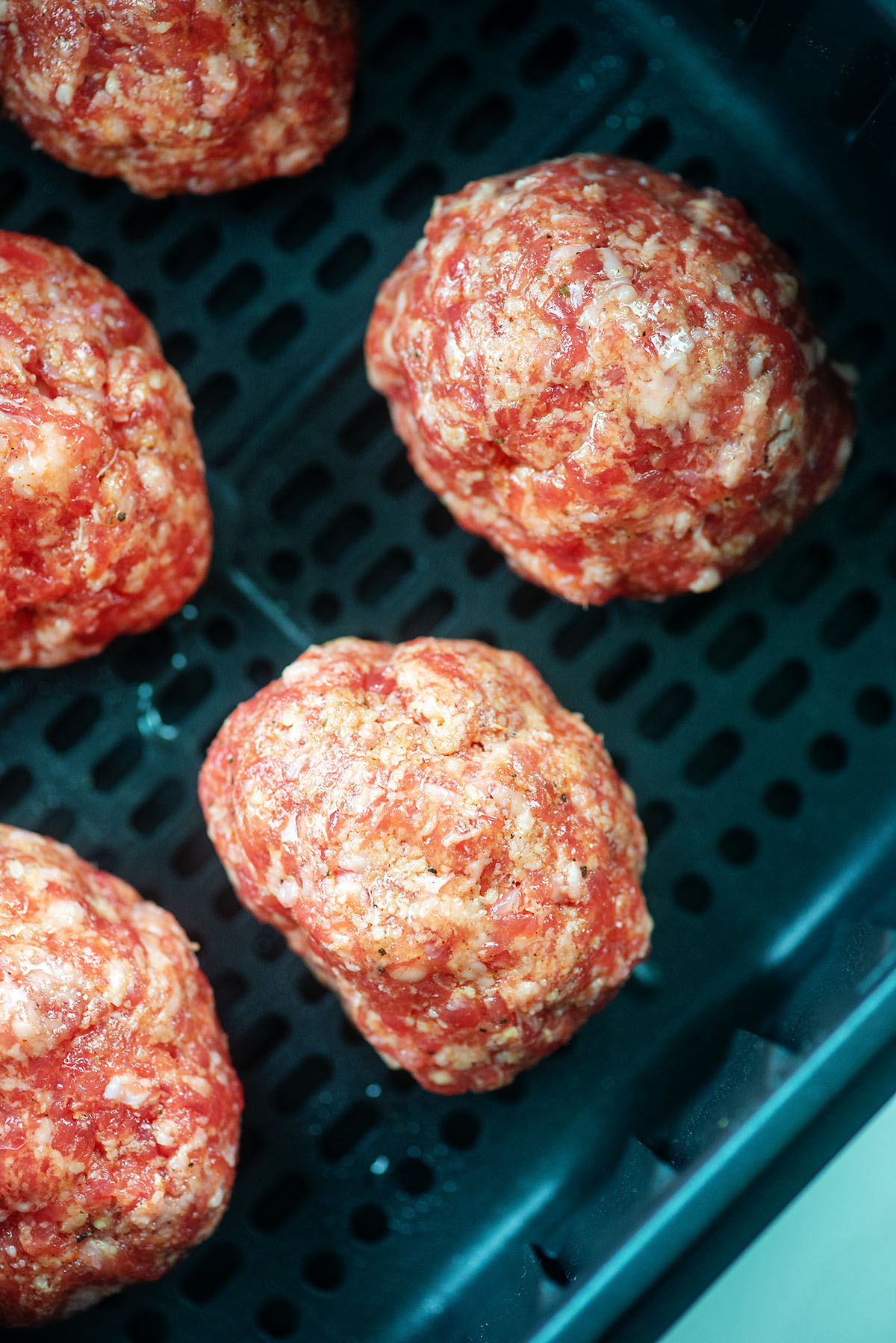 boiled eggs wrapped in sausage and placed in an air fryer basket.