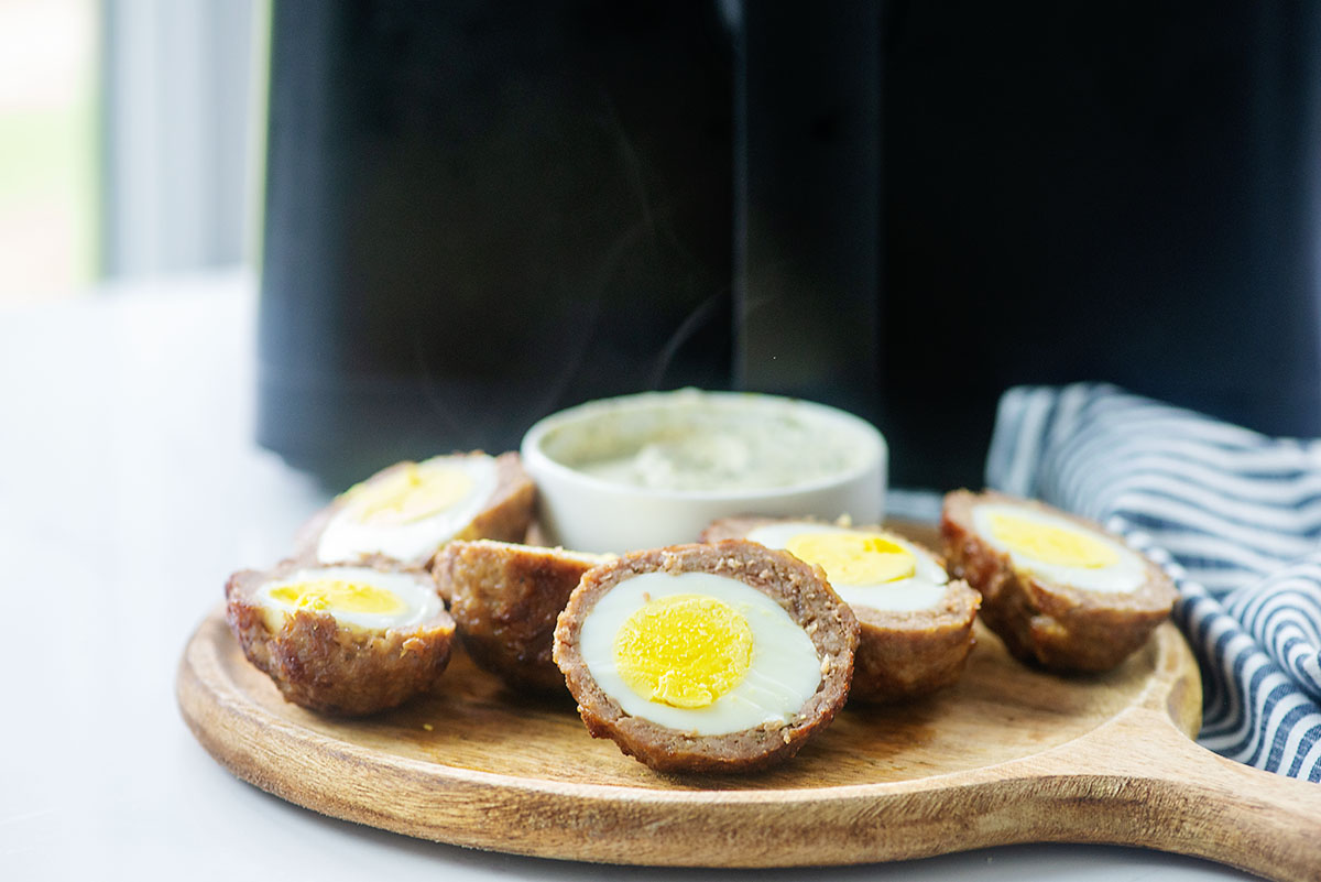 sliced eggs wrapped in sausage on cutting board with dip.