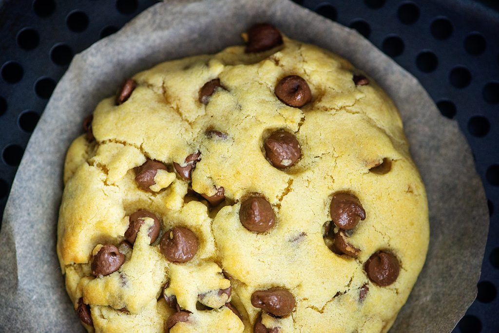 A close up of a chocolate chip cookie on parchment paper.
