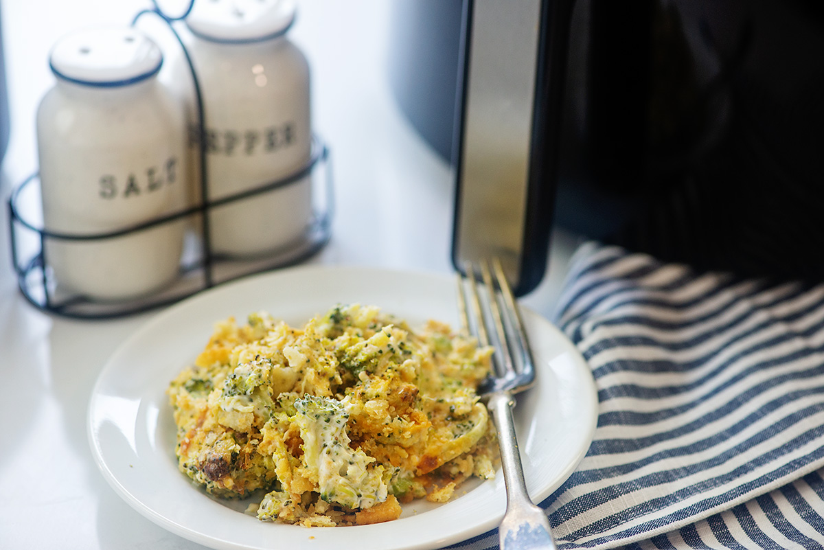 Cheesy broccoli casserole on a white plate in front of an air fryer