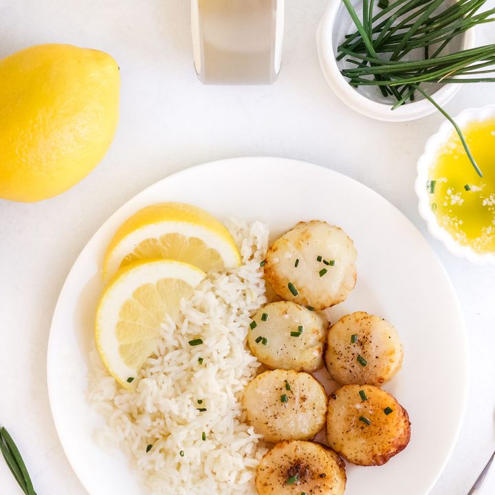 overhead view of rice, scallops, and lemons on a white plate