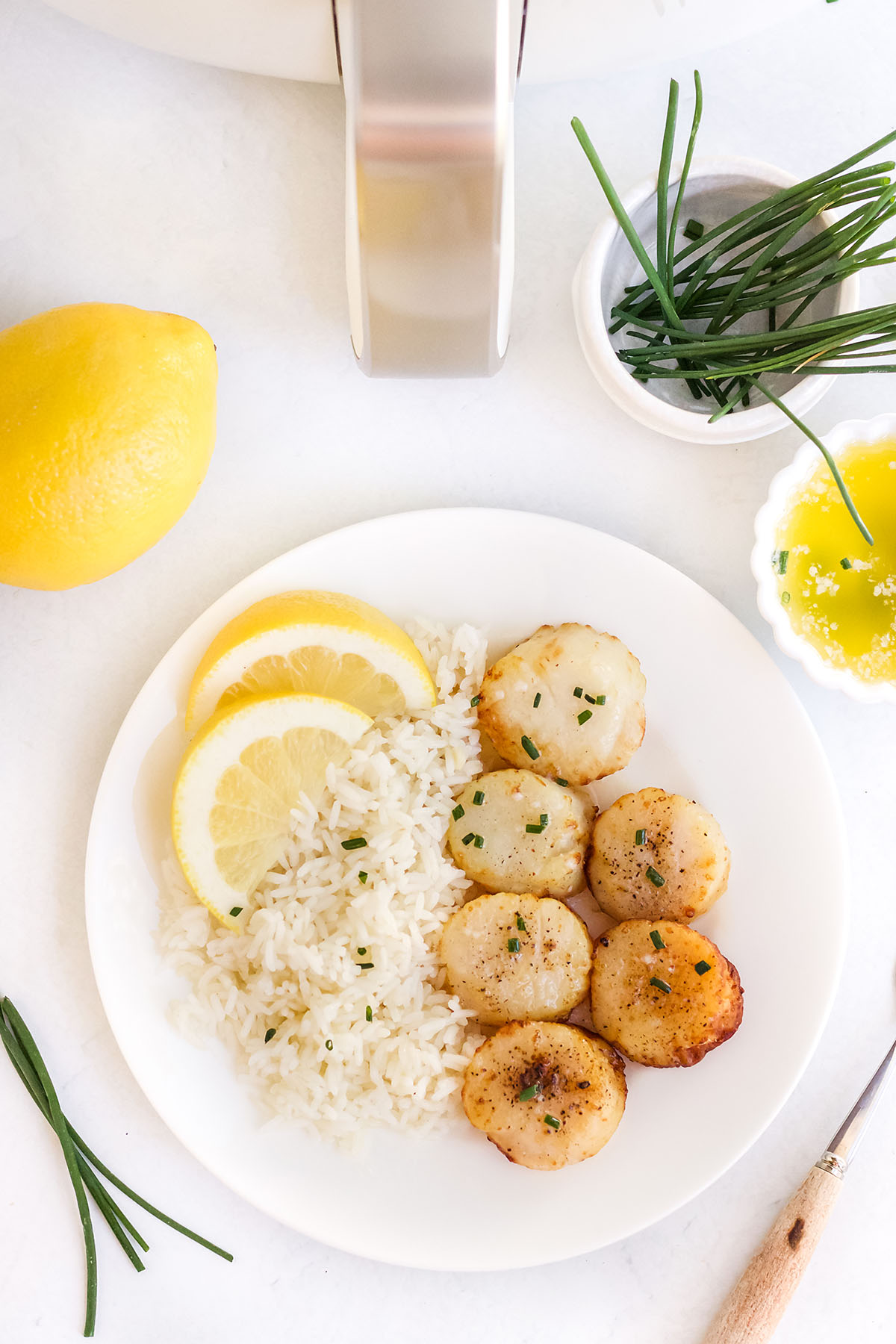 overhead view of rice, scallops, and lemons on a white plate