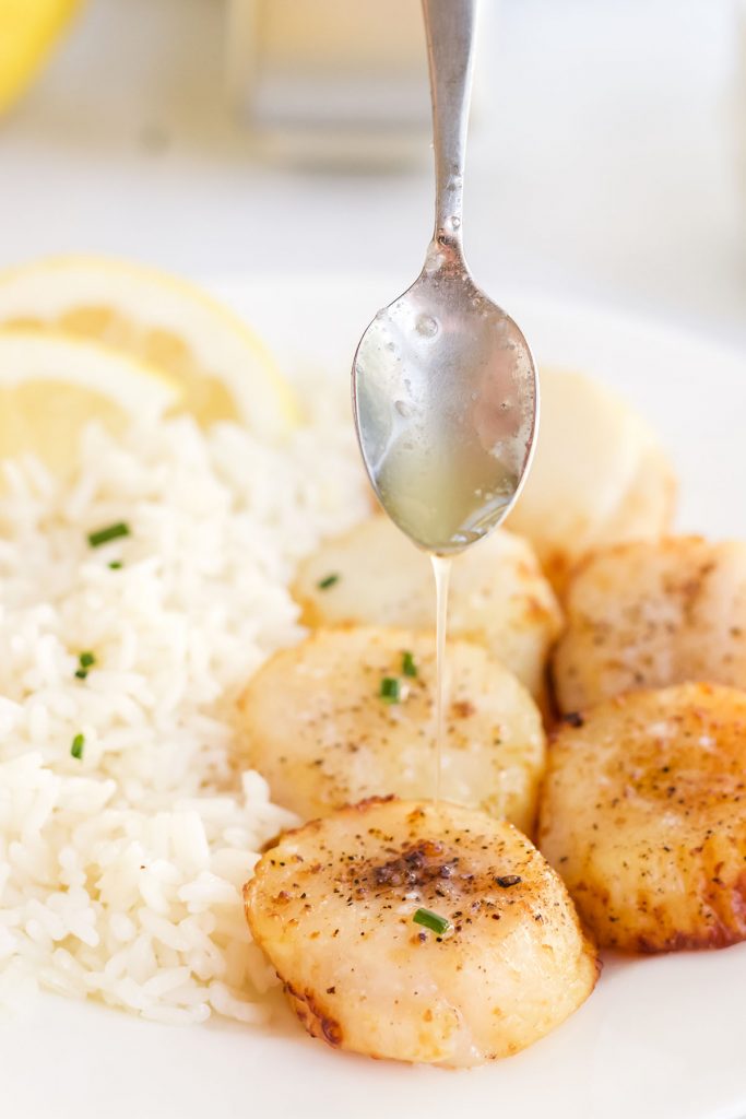 A spoon drizzling lemon garlic on top of a scallop