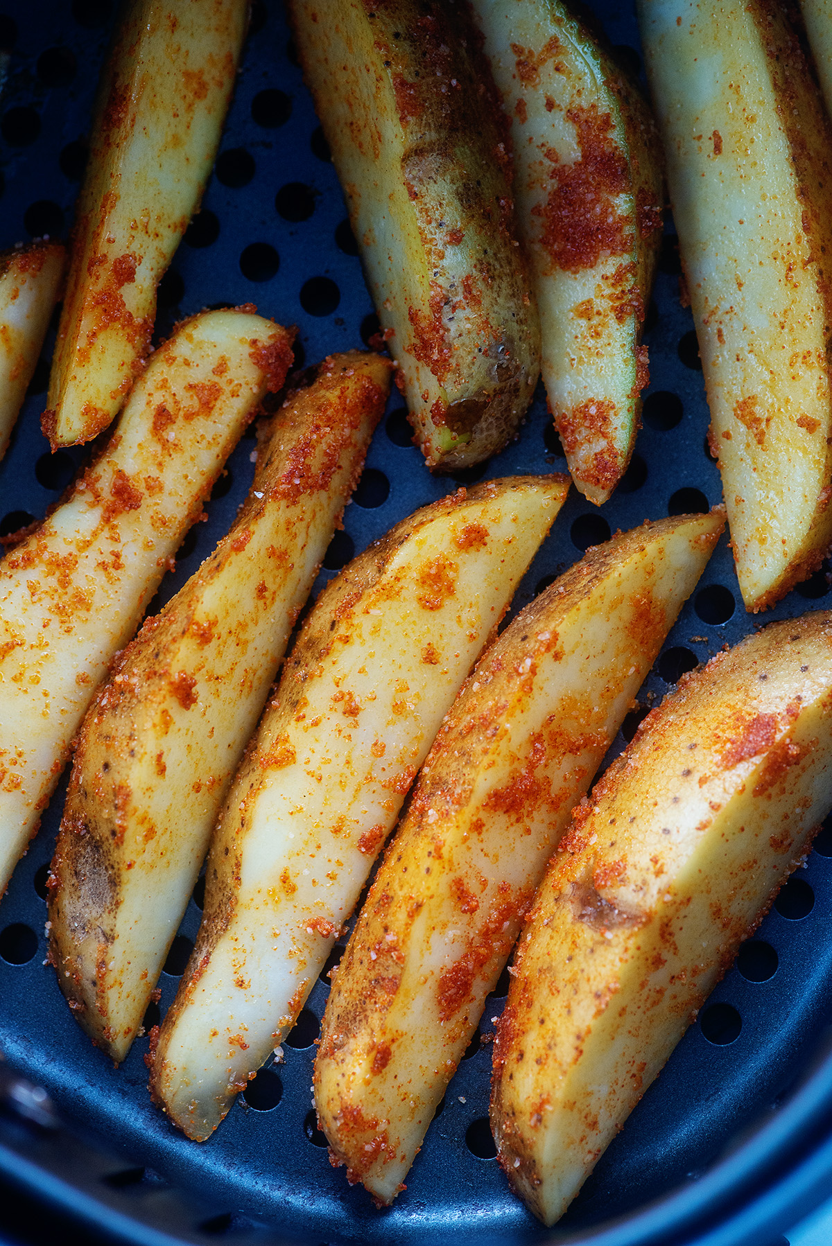 Seasoned potato wedges in an air fryer basket