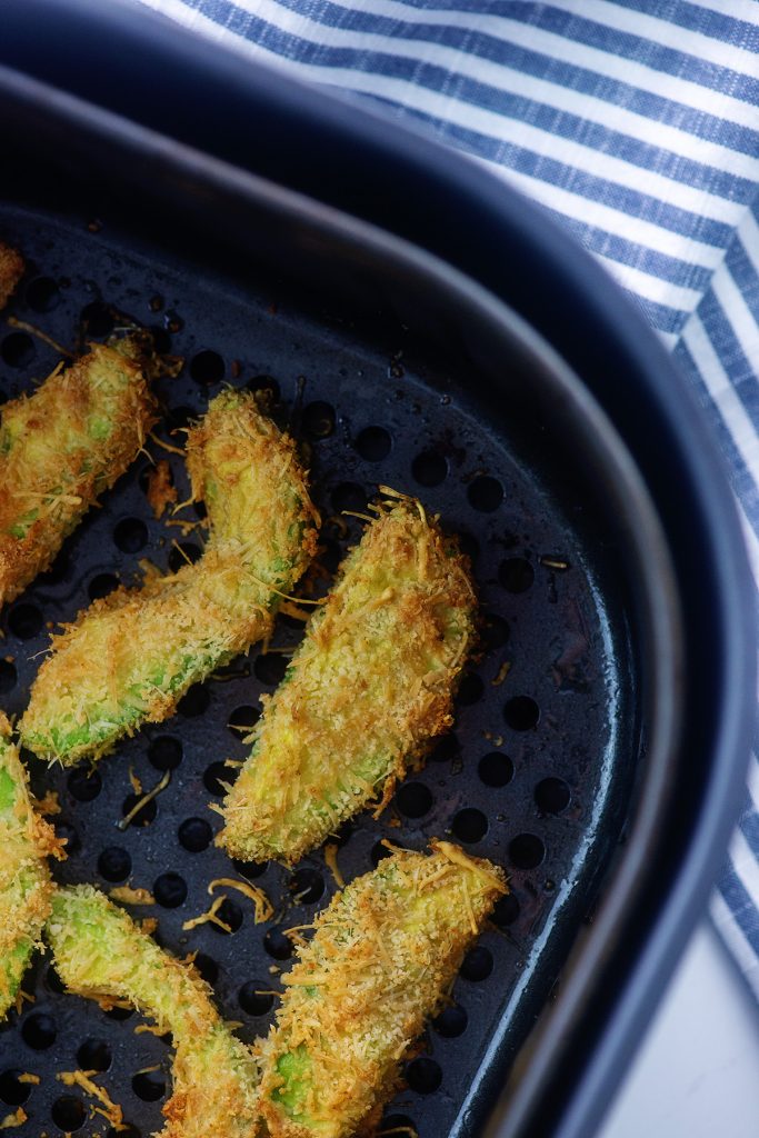 avocado fries spread out in an air fryer basket