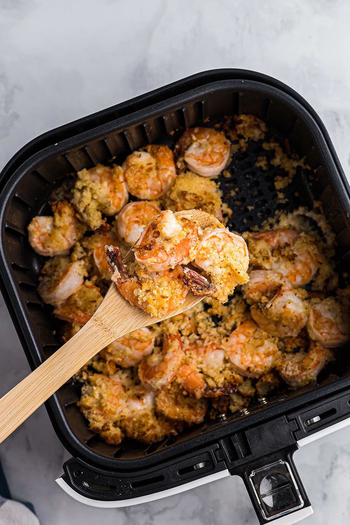 A wooden spoon scooping shrimp out of an air fryer basket