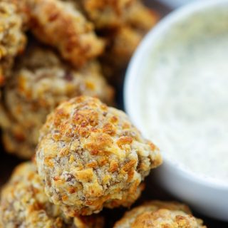 A close up of sausage balls next to a cup of dill dip