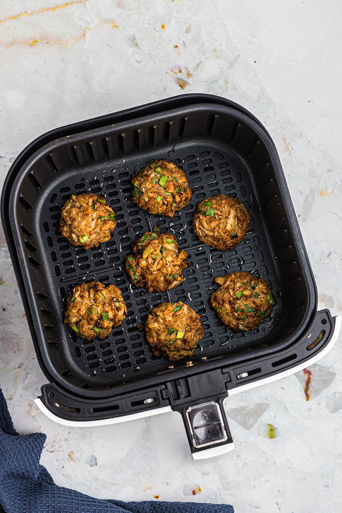 OVerhead view of 7 crab cakes cooked in an air fryer basket.