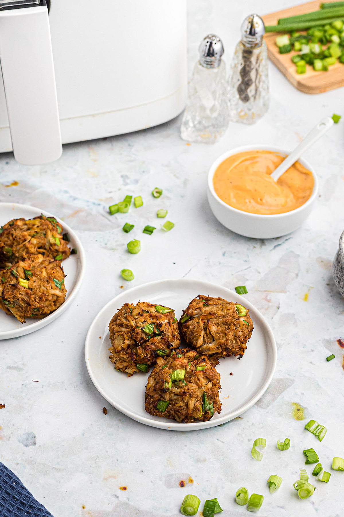 Three crab cakes on a plate in front of an air fryer.