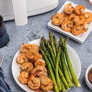 Two plates of shrimp in front of a white air fryer