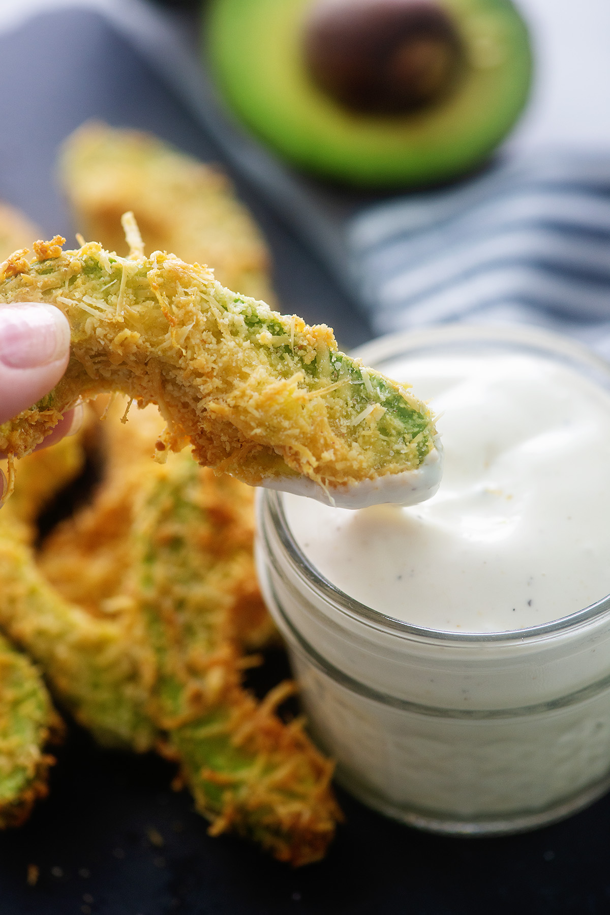 An avocado fry being dipped into ranch dressing