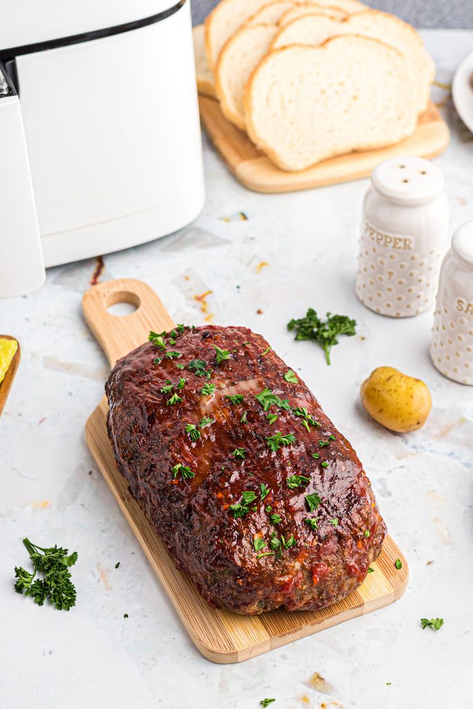 A glazed meatloaf on a small cuttingboard next to a salt and pepper shaker
