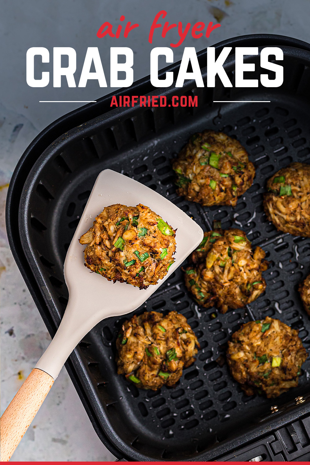 A spatula scooping a crab cake out of an air fryer basket