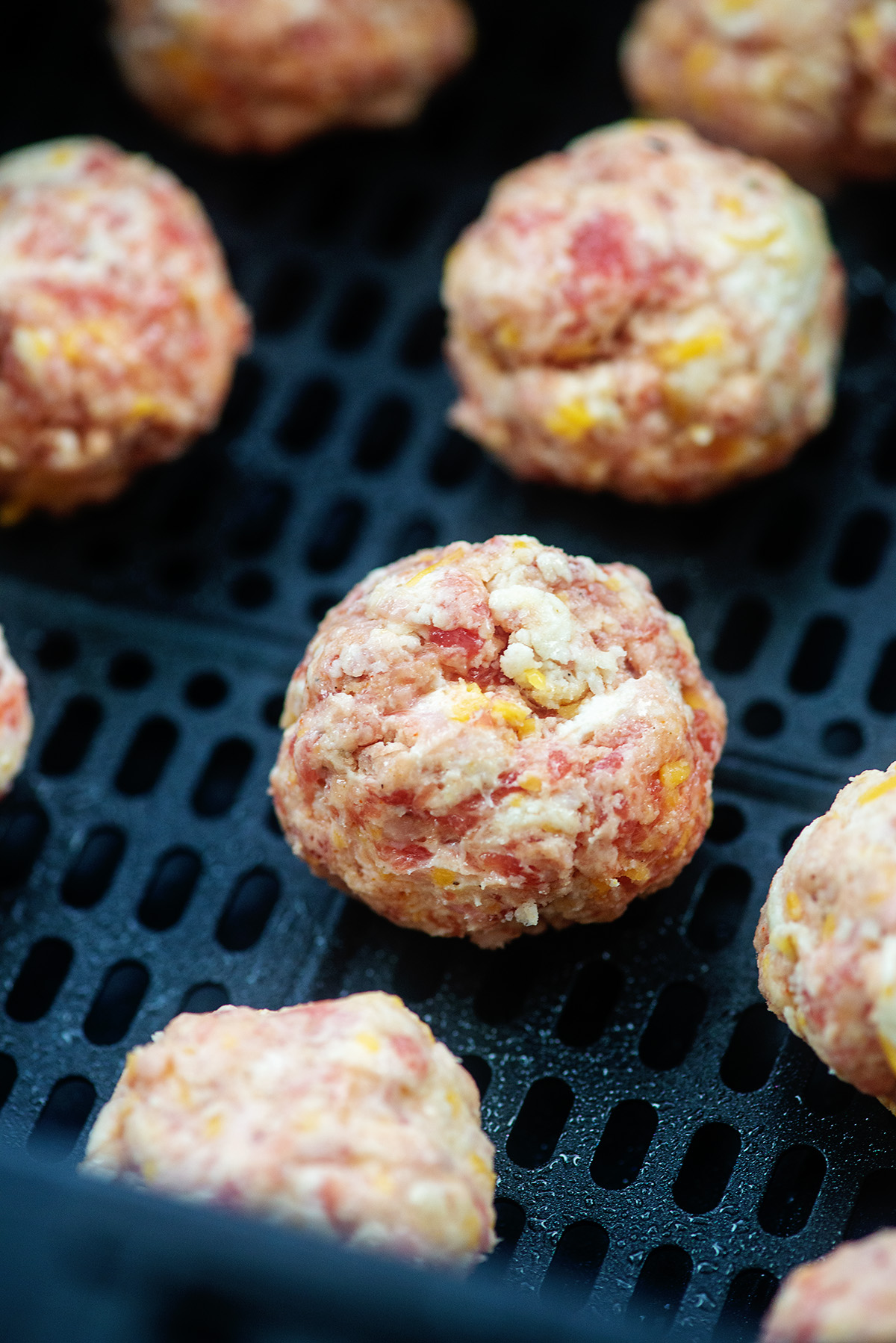 raw meatballs spread out in an air fryer basket