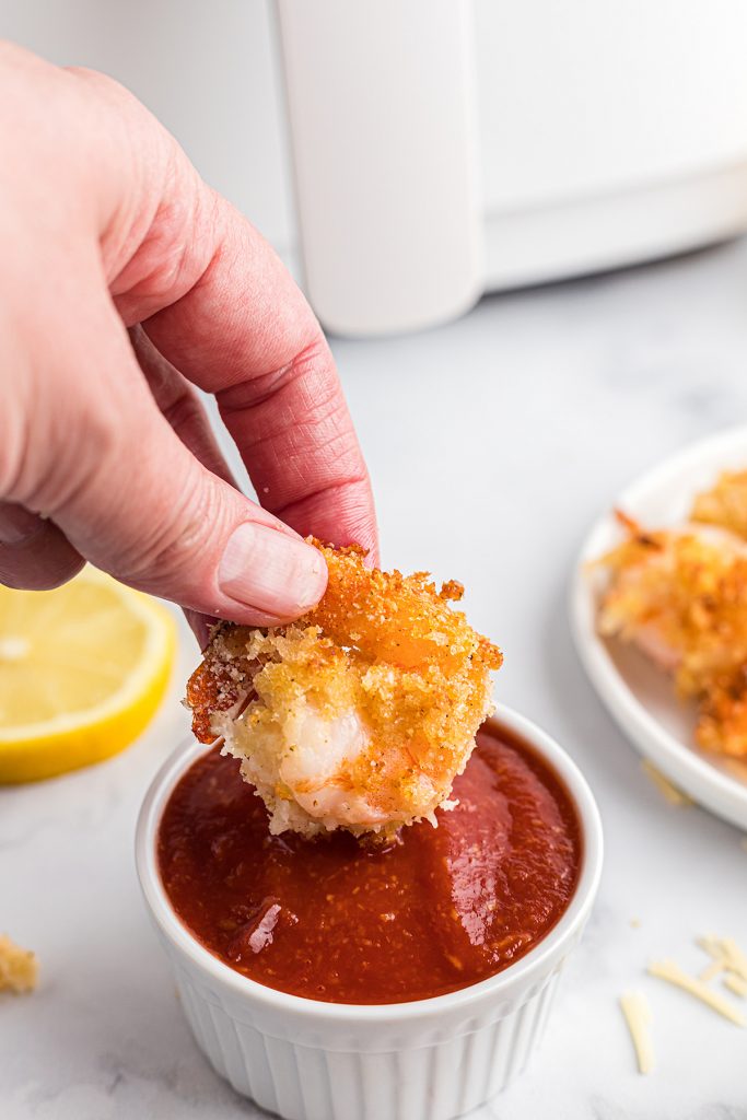 Fried shrimp being dipped in cocktail sauce.