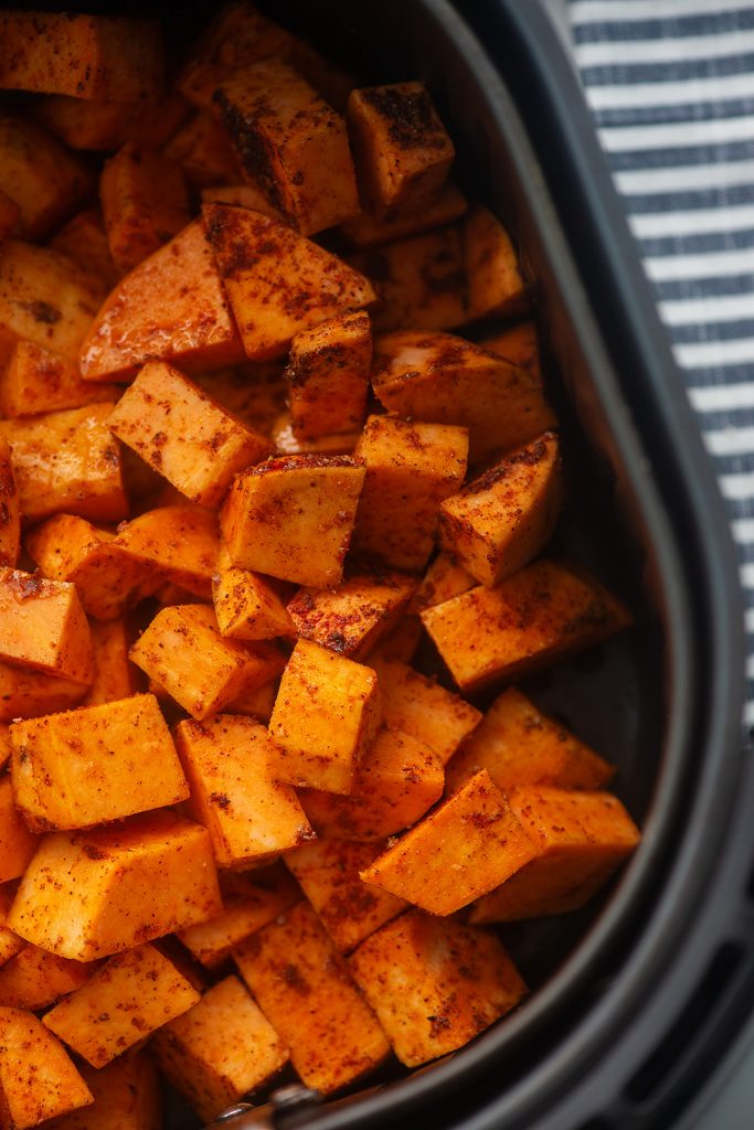 Close up of seasoned sweet potato cubes in an air fryer basket.