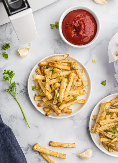 overhead view of two plates of french fries next to a cup of ketchup