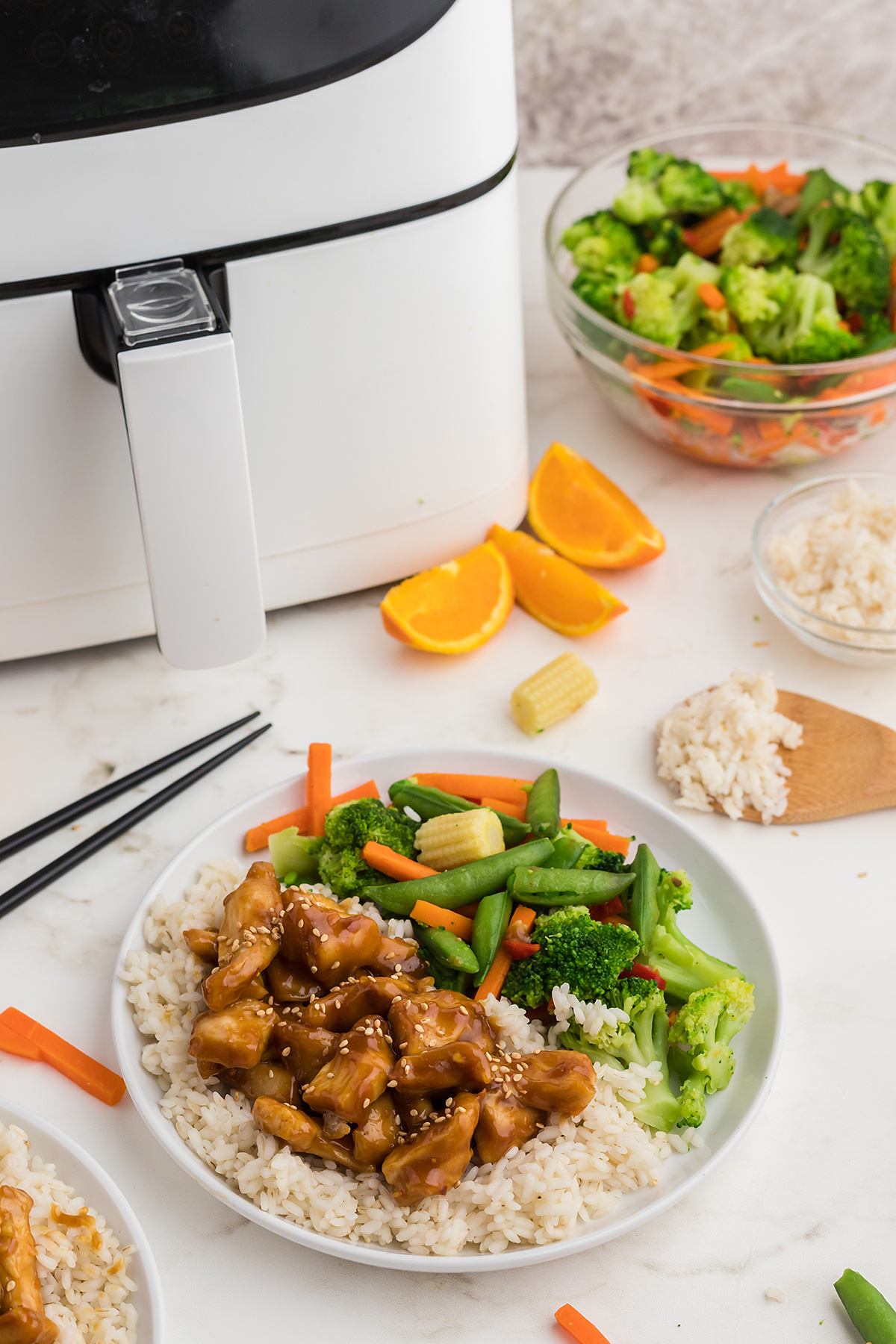 a white air fryer behind a plate of Chinese food