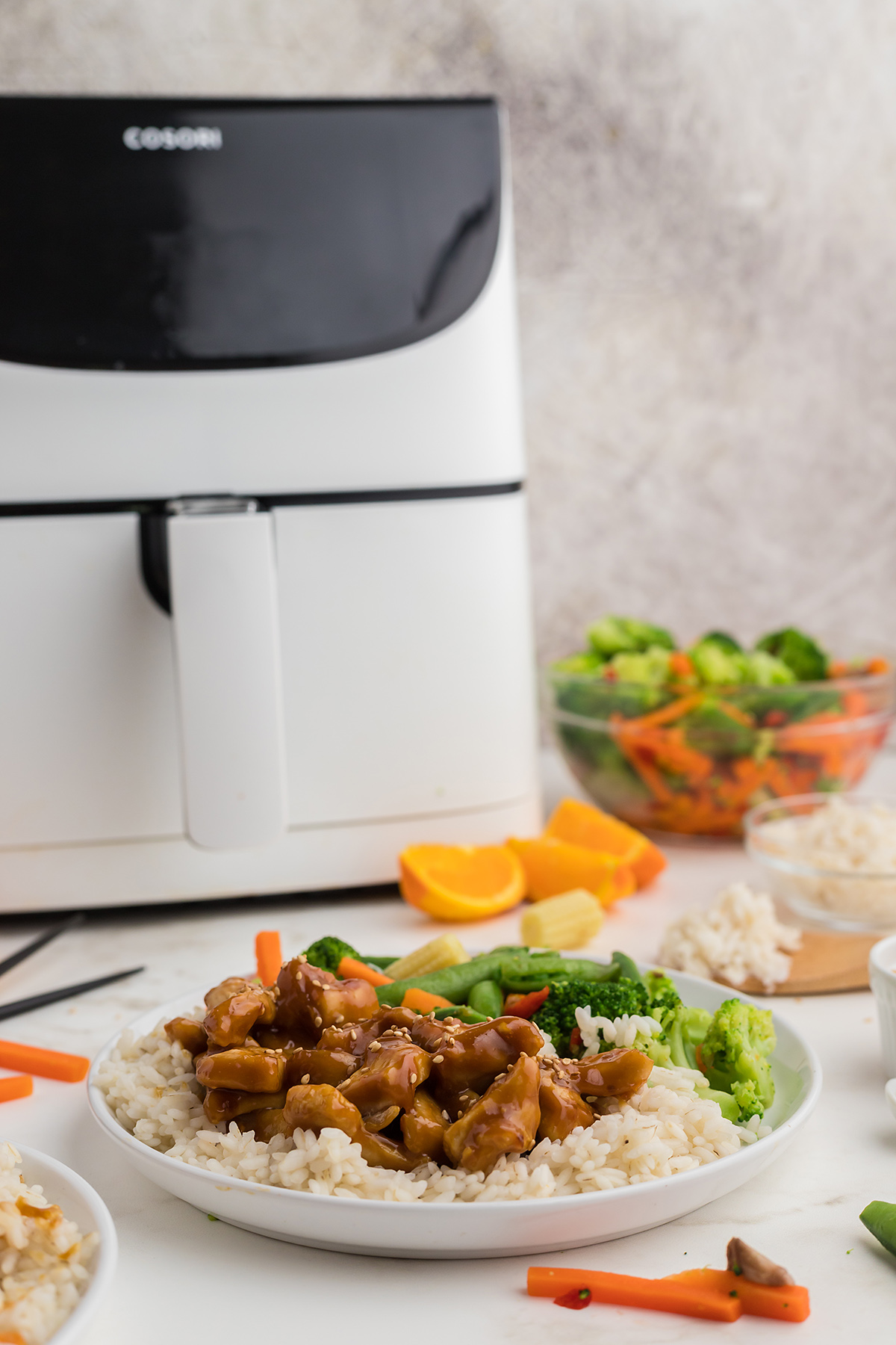 A plate of orange chicken in front of an air fryer