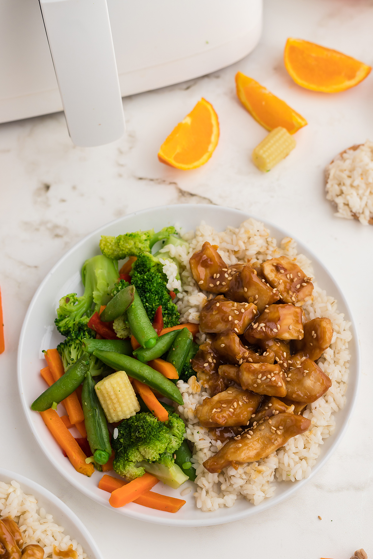 oeverhead view of a plate e of orange chicken in front of an air fryer